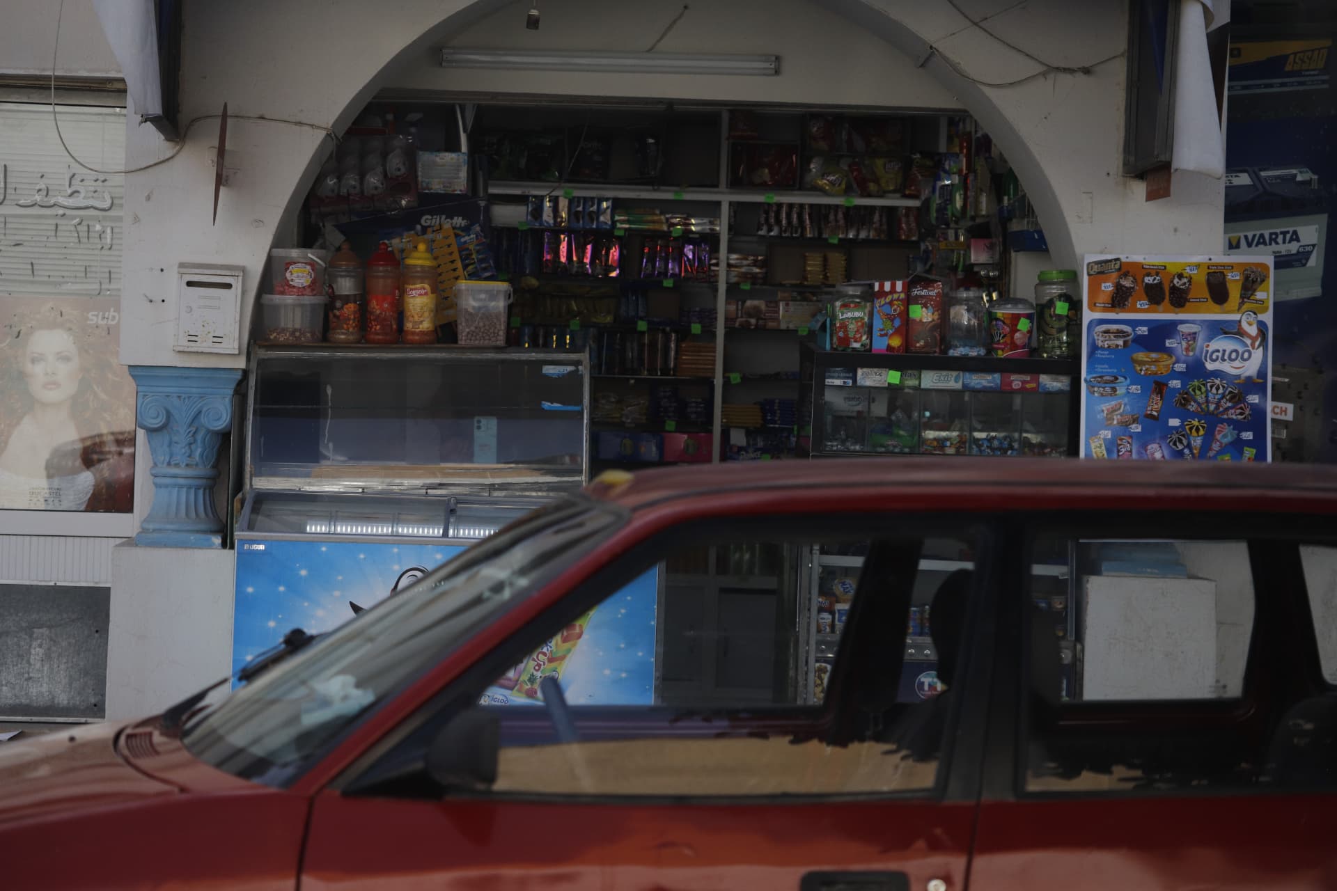 Red car passing a small neighborhood shop